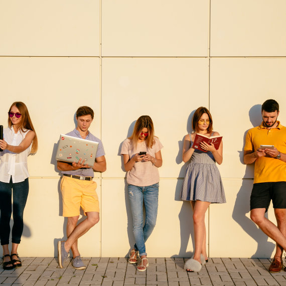 Beautiful young students are using gadgets, reading book and smiling, standing over wall background